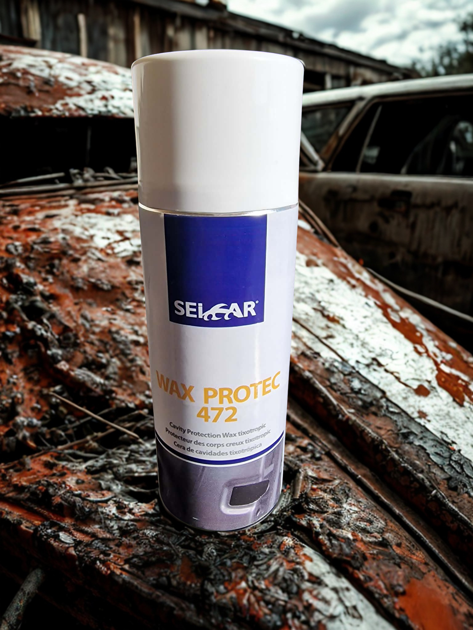 Close-up of a white spray can labeled Wax Protec 472 in a rusted junkyard setting.